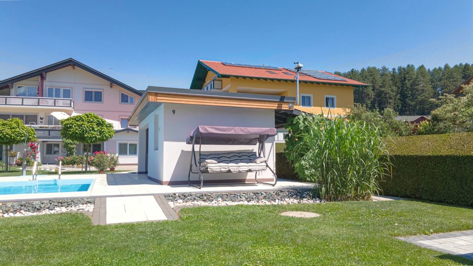Badehütte mit Hollywoodschaukel, Ziergräser und Pool, dahinter das Nachbarhaus