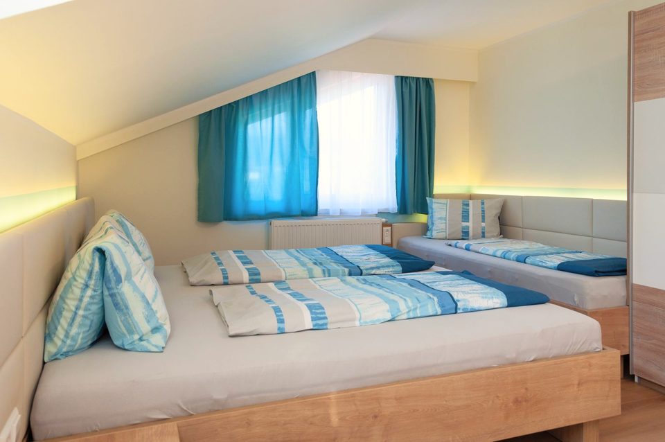 Vierbettzimmer mit blau-weißer Bettwäsche unter der Dachschräge