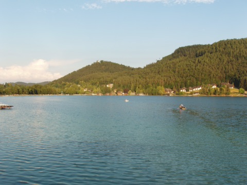 Ruderboot auf dem Klopeiner See, dahinter bewaldete Hügel und Häuser am Ufer