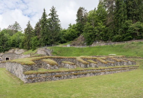 Freigelegte Steinmauern des römischen Tempels im Archäologischen Park Magdalensberg, dahinter Wiese und Nadelwald