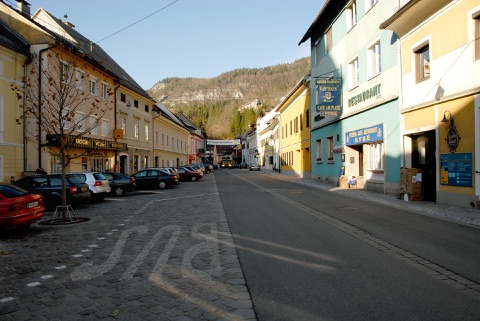 Hauptplatz von Bad Eisenkappel mit bunten Bürgerhäusern und Gasthäusern, im Hintergrund bewaldete Berge