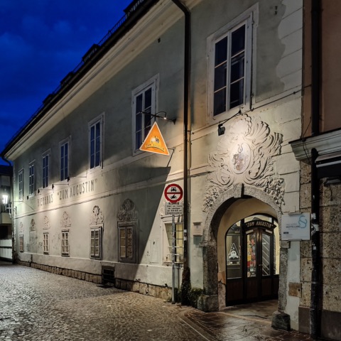 Fassade des Bierhauses „Zum Augustin“ in der Pfarrhofgasse in Klagenfurt am Abend, mit Wirtshausschild und Steinportal