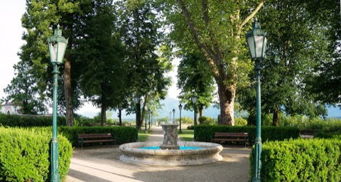 Brunnen zwischen alten Bäumen und Laternen im Bürgerlustpark Völkermarkt