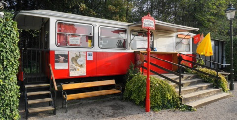 Rot-weißer Straßenbahnwagen des Buffets „Zur Tramway“ mit Haltestellenschild am Lendkanal