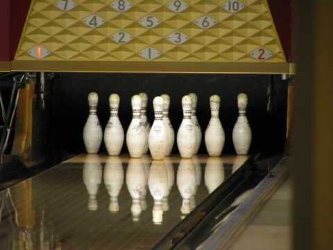 Zehn weiße Bowlingkegel am Ende einer glänzenden Holzbahn, darüber eine Anzeige mit den Kegelnummern