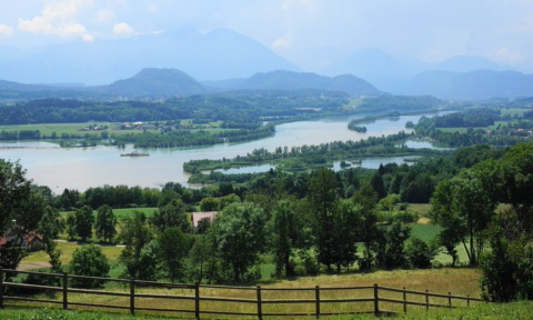 Blick von einer Anhöhe auf den Völkermarkter Stausee der Drau mit bewaldeten Inseln und Seitenarmen, dahinter Hügel und Berge