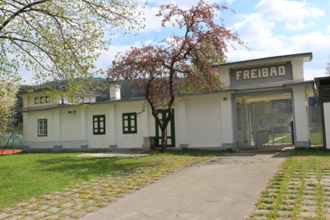 Weißes historisches Eingangsgebäude des Freibads Bleiburg mit Schriftzug „Freibad“ im Frühling