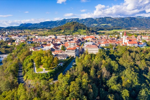 Luftaufnahme der Stadt Völkermarkt mit Stadtpfarrkirche und bewaldetem Hang, im Hintergrund die Saualpe