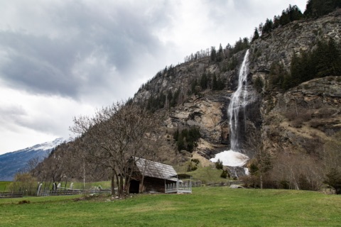Fallbach-Wasserfall stürzt über eine hohe Felswand im Maltatal, davor eine Wiese mit Holzhütte