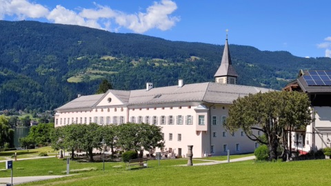 Das Stift Ossiach mit Kirchturm vor bewaldeten Hängen am Ossiacher See – von hier geht man durch den Stiftshof hinauf zum Familywald