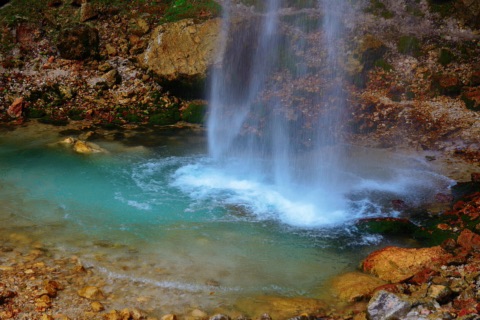 Wildensteiner Wasserfall: Wasser stürzt in ein türkisfarbenes Becken zwischen Felsen und Herbstlaub