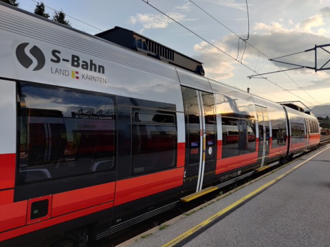 Rot-silberner Triebzug der S-Bahn Kärnten mit der Aufschrift „S-Bahn Land Kärnten“ an einem Bahnsteig im Abendlicht