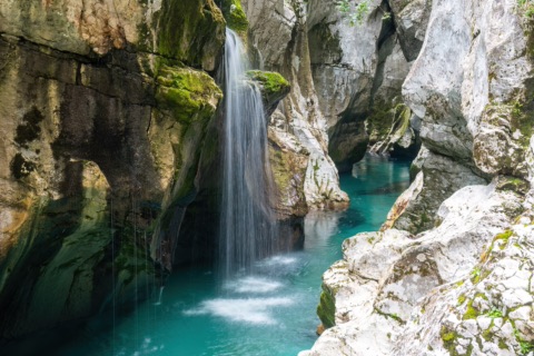 Kleiner Wasserfall stürzt in ein türkisgrünes Becken zwischen hellen Kalkfelsen der Soča-Schlucht
