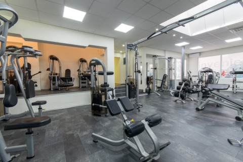 Heller Fitnessraum mit Kraftgeräten, Hantelbänken und Kurzhanteln