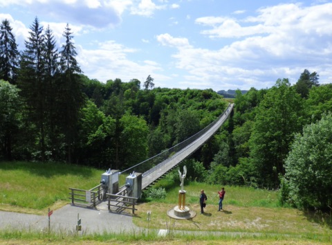 Hängebrücke Santa Lucia über den bewaldeten Feistritzgraben, im Vordergrund eine Skulptur am Brückenkopf
