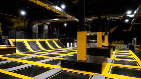 Leere Trampolinhalle mit vielen aneinandergereihten Trampolinfeldern, schrägen Wandtrampolinen und gepolsterten Blöcken in Gelb und Schwarz