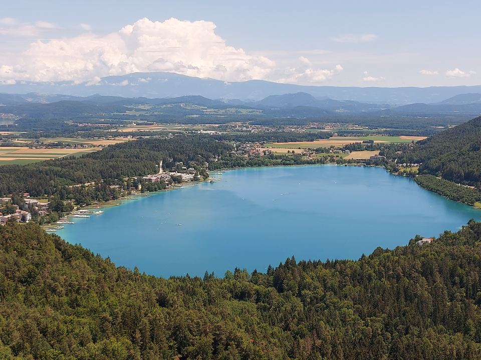 Blick vom Kitzelberg über den türkisen Klopeiner See, umrahmt von Wald und Feldern – bis zu den Bergen am Horizont