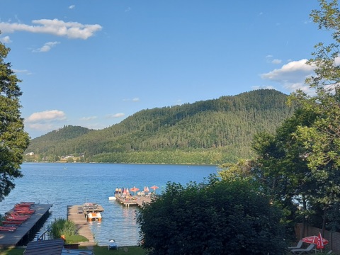 Badestege mit Liegen und Sonnenschirmen am Klopeiner See, dahinter der bewaldete Höhenzug der Gracarca