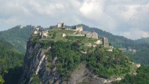 Burgruine Griffen auf einem steilen, bewaldeten Felsen, dahinter bewaldete Hügel