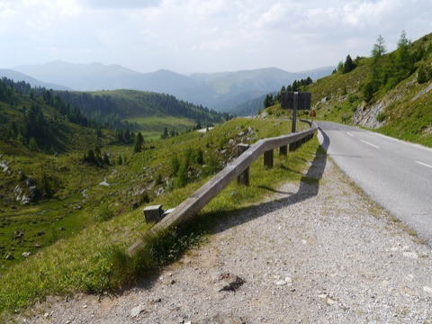 Kurvige Nockalmstraße mit Holzleitplanke vor grünen Almen und den Nockbergen