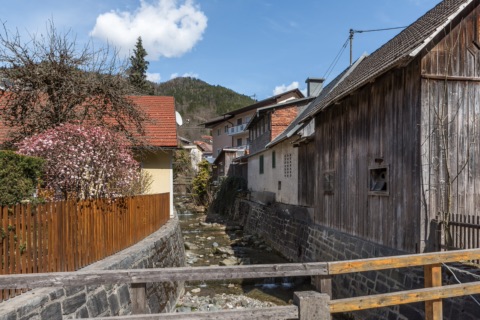 Der Lobnigbach fließt zwischen alten Häusern und Holzstadeln durch Bad Eisenkappel