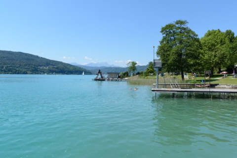 Badesteg und Liegewiese mit großen Bäumen im Parkbad Krumpendorf am türkisen Wörthersee