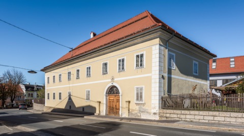 Ehemaliger Propsthof an der Bleiburger Straße in Eberndorf, ein zweigeschossiges gelbes Gebäude mit rotem Walmdach, Rundbogenportal und Holztür