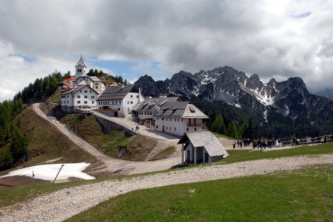 Wallfahrtskirche und Häuser auf dem Monte Lussari, dahinter die schroffen Gipfel der Julischen Alpen