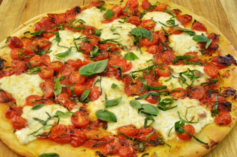 Pizza Margherita mit Kirschtomaten, Mozzarella und frischem Basilikum auf einem Holzbrett