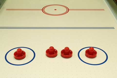 Vier rote Airhockey-Schläger auf einer hellen Airhockey-Spielfläche mit roter Mittellinie und blauen Kreismarkierungen
