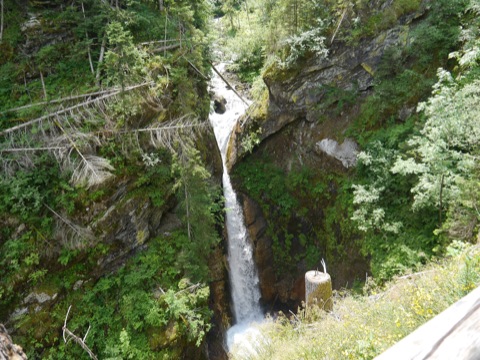 Wasserfall des Raggabachs in einer bewaldeten Felsschlucht, im Vordergrund das Geländer des Stegs