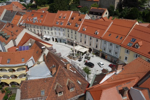Blick vom Kirchturm auf den Hohen Platz in der Wolfsberger Altstadt mit Säule, Bürgerhäusern mit roten Ziegeldächern und Gastgarten mit Sonnenschirmen
