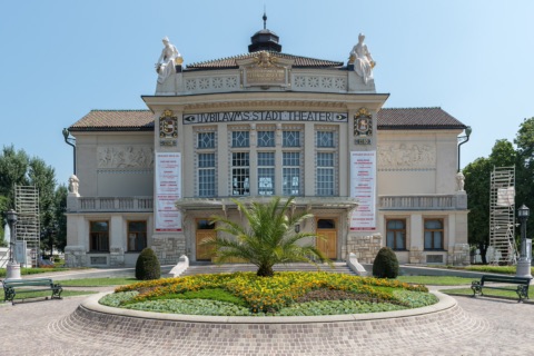 Jugendstilfassade des Stadttheaters Klagenfurt mit der Inschrift Jubiläums-Stadt-Theater und Blumenbeet davor
