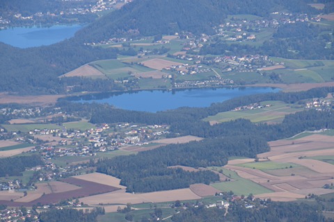 Blick vom Obir hinunter auf den Turnersee mit bewaldetem Südufer, Feldern und Dörfern, dahinter der Klopeiner See