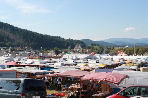 Der Bleiburger Wiesenmarkt: unzählige Marktstände und Zelte unter blauem Himmel, dahinter Riesenrad und Berge