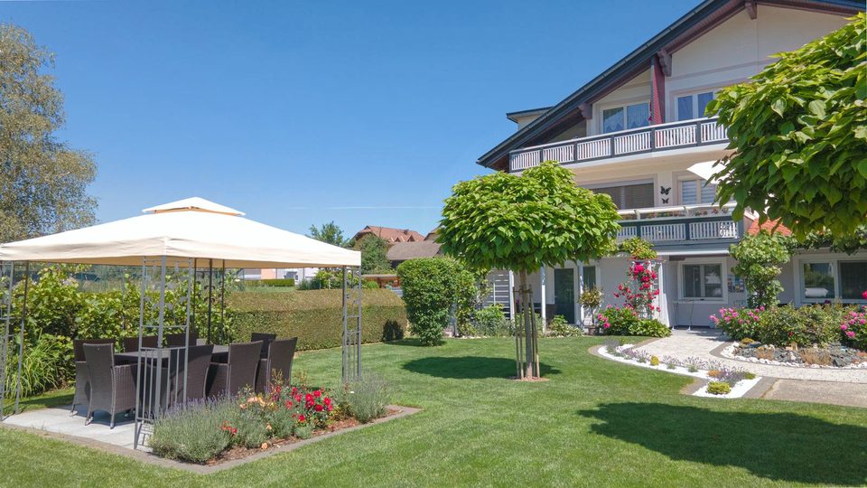 Weißer Pavillon mit Sitzgruppe im Garten neben Blumenbeeten