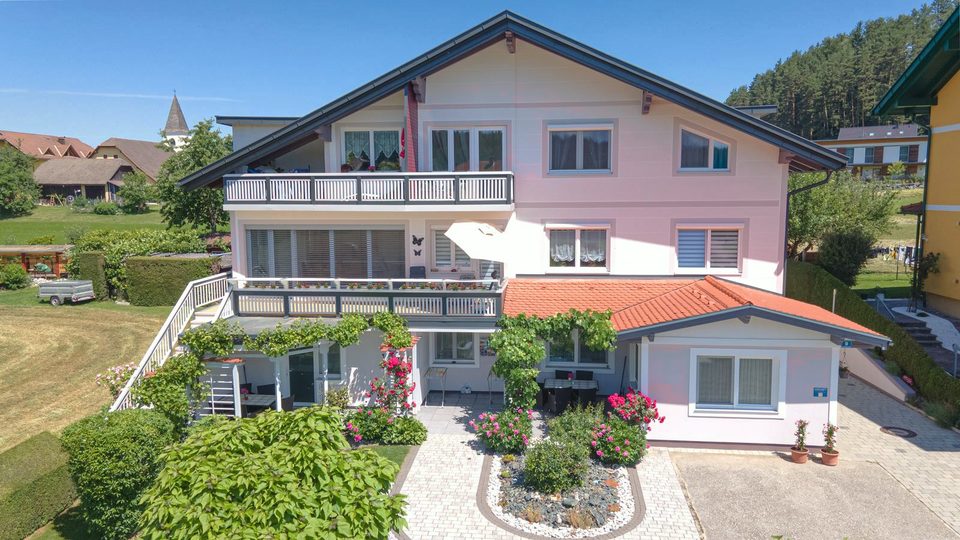 Das Ferienhaus Jernej von vorne: zartrosa Fassade, anthrazitfarbene Balkone und rotes Ziegeldach am Anbau