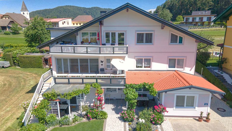 Vorderansicht des Hauses mit Rosenpergola, im Hintergrund der Kirchturm und bewaldete Hügel