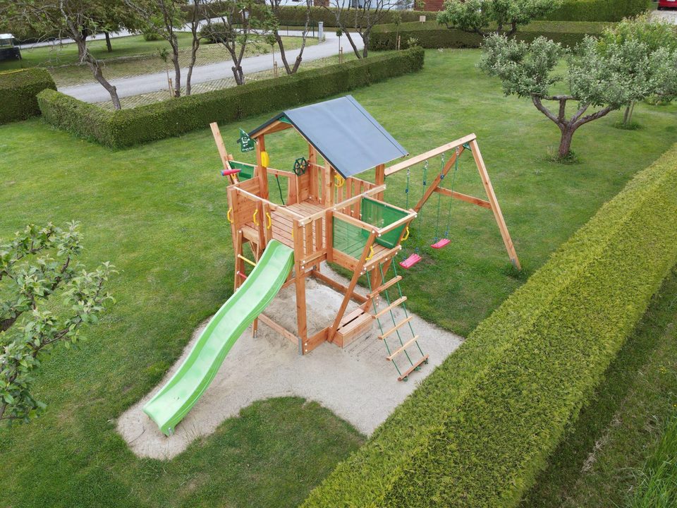 Spielturm mit Rutsche aus der Vogelperspektive, umgeben von Hecken und Obstbäumen