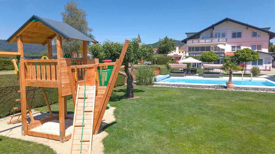 Holz-Spielturm mit Kletterwand, dahinter Pool und Haus