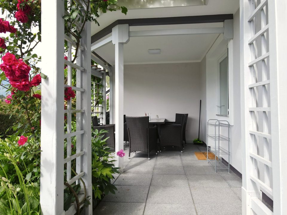 Überdachter Sitzplatz hinter der weißen Rosenpergola