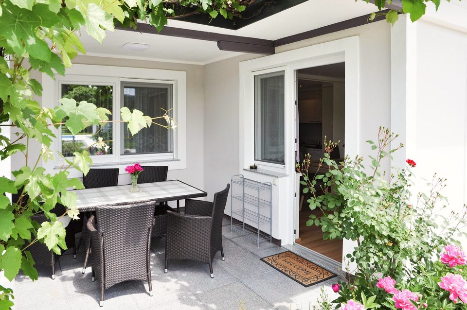 Überdachte Terrasse mit Rattan-Sitzgruppe, Weinlaub und Rosen