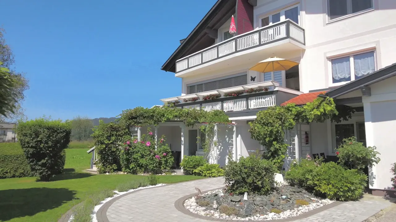 Das Haus von der Seite mit Balkonen, Pergola und Garten
